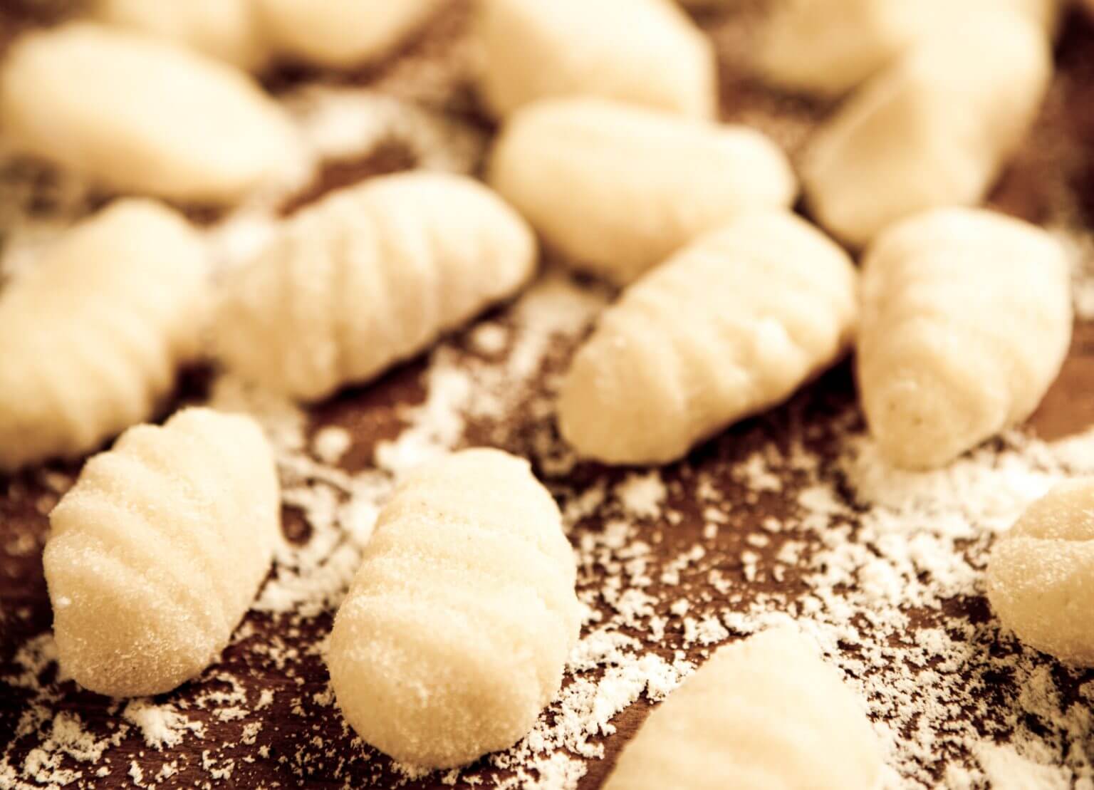 Handmade gnocchi coated in flour resting on a wooden cutting board.