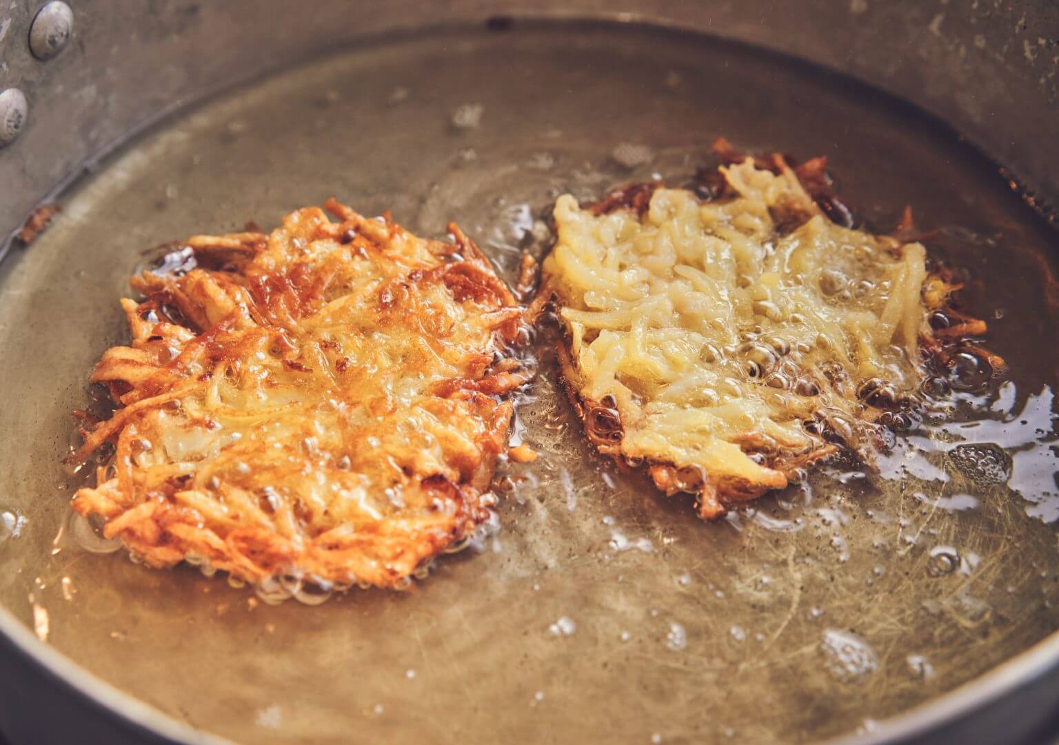 Two potato pancakes decadently frying in a pan of glistening oil.
