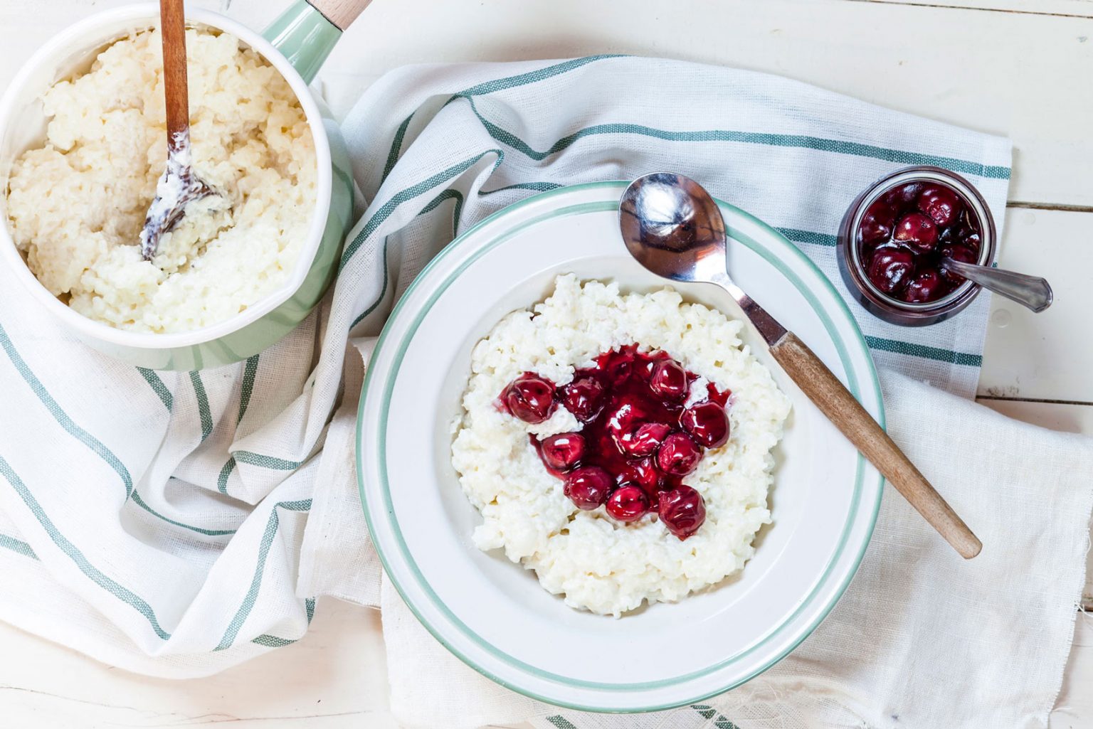 A white bowl with teal trim filled with Risalamande topped with cherry sauce.