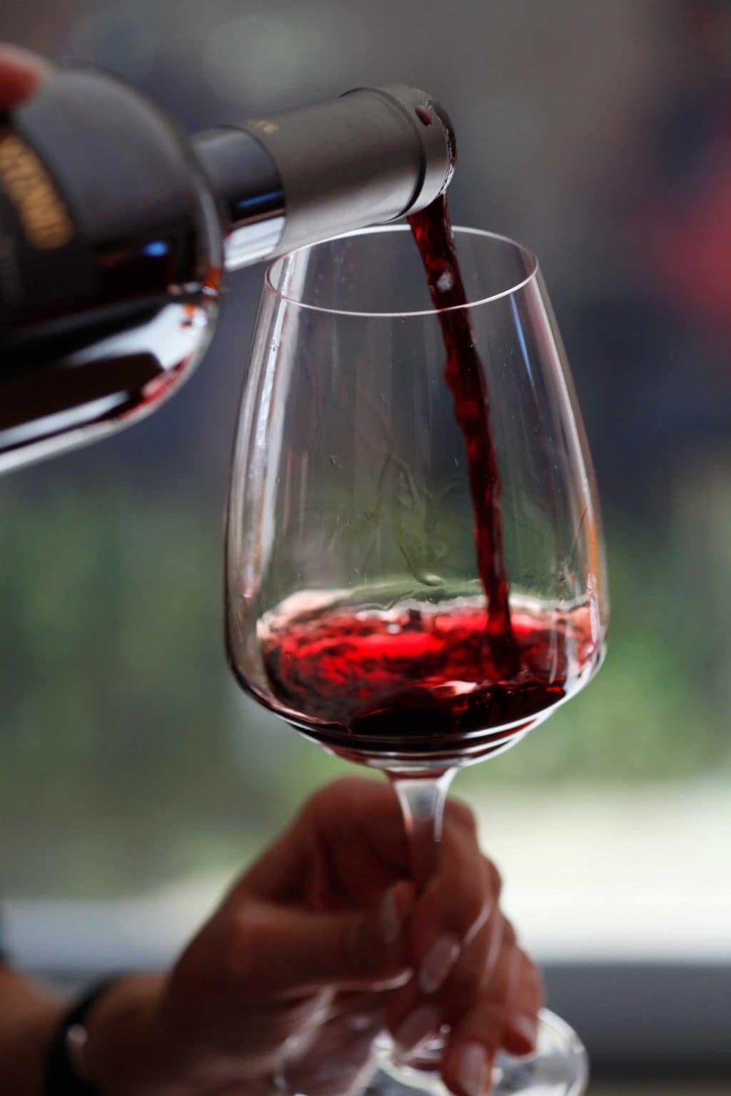 A person filling a clean, clear wine glass with red wine.