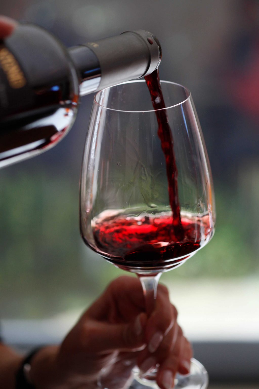 A person filling a clean, clear wine glass with red wine.