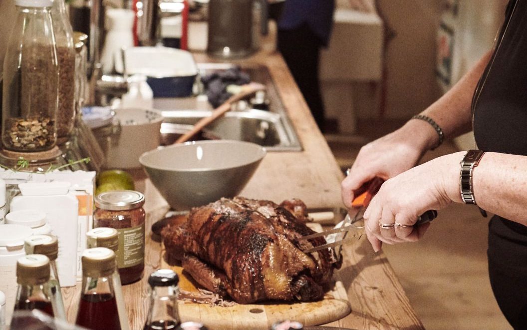 A person slicing a roasted duck on a wooden cutting board.
