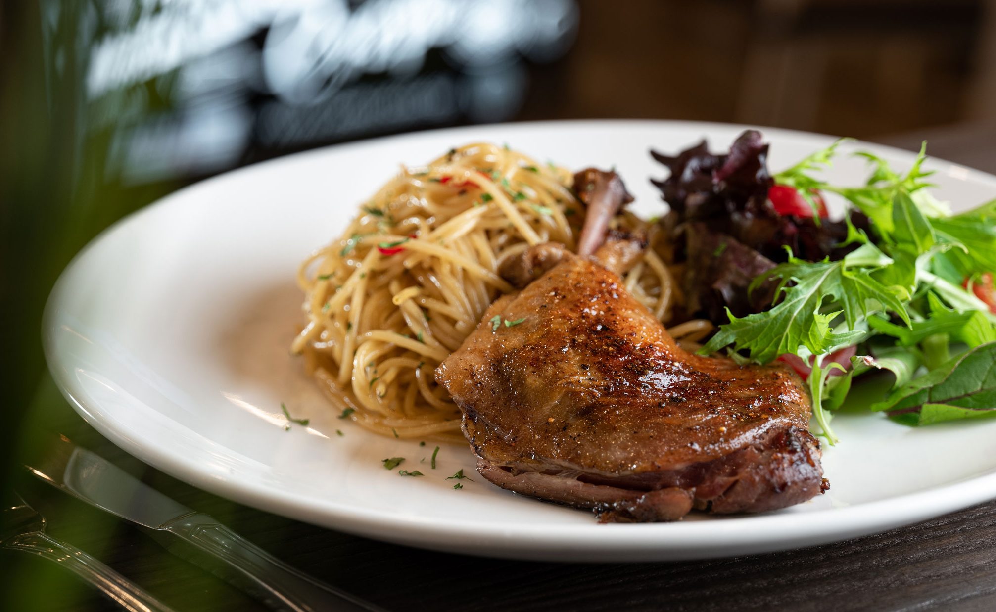 A white dinner plate filled with duck, spaghetti and salad.