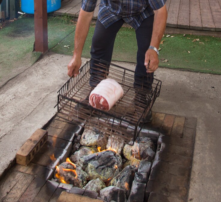 A man preparing Maori hangi: food wrapped in wet cloth in a metal basket.