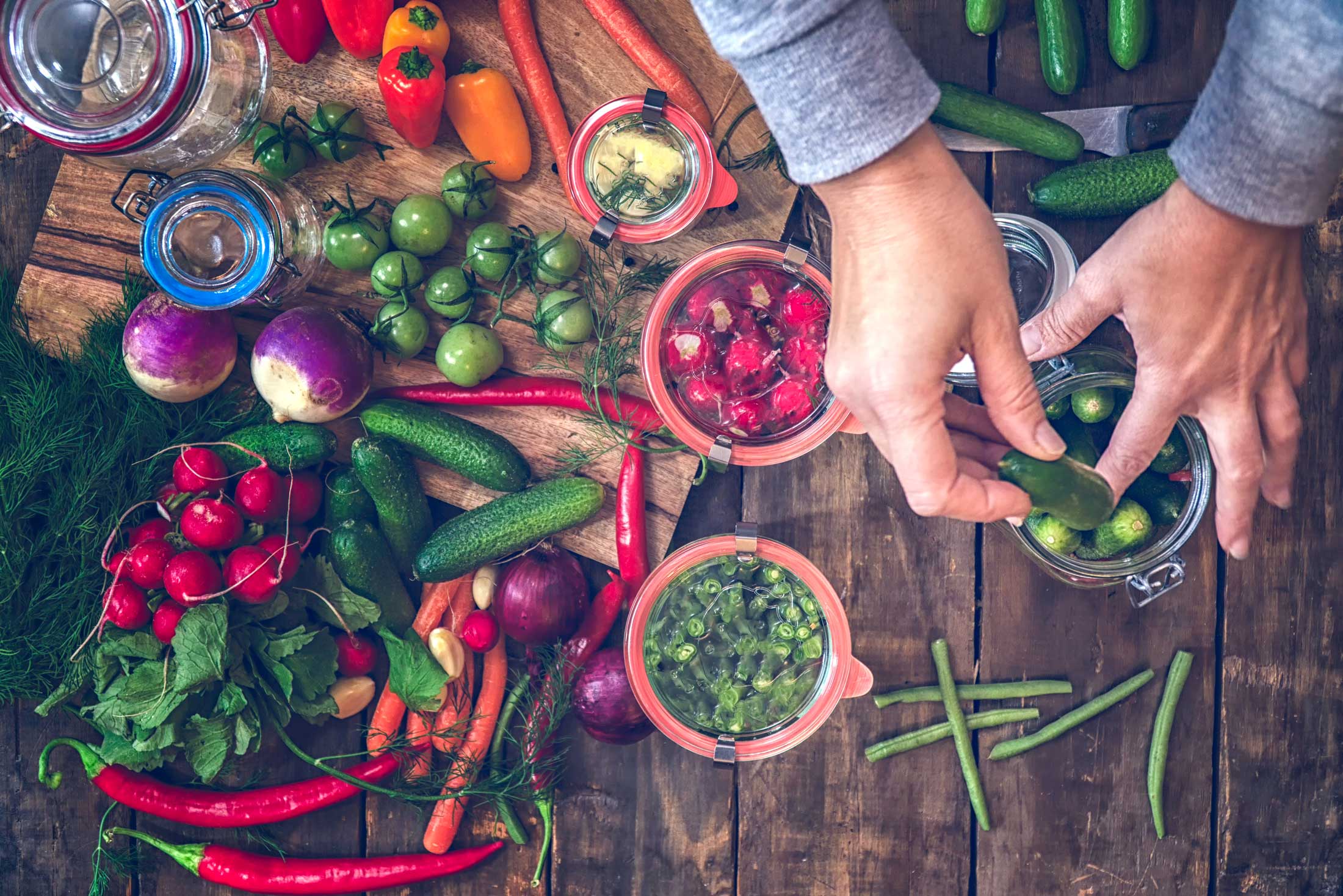 A variety of colorful vegetables strewn about the table to be pickled in glass jars.