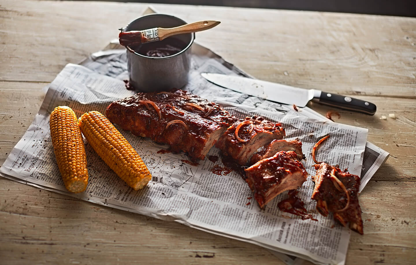 A sliced rack of barbeque ribs resting on newspaper.