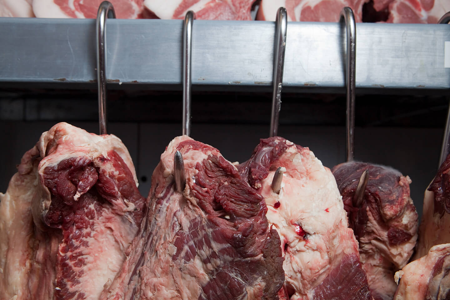 Raw, fresh meat hanging from stainless steel meat hooks.