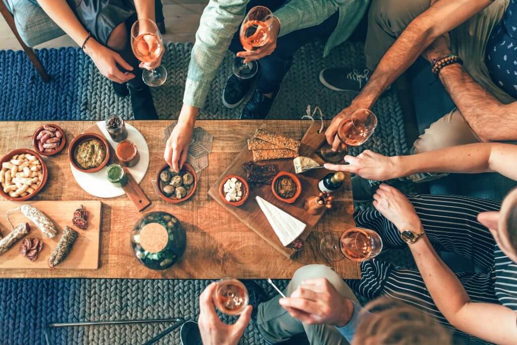 A gathering of friends sitting around a coffee table sharing small eats and sipping wine.