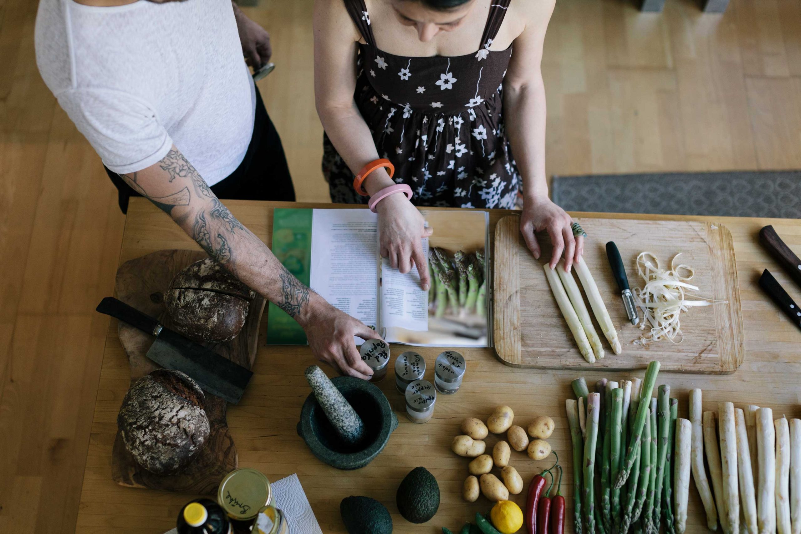 Two people reading through an asparagus recipe in a cook book together.
