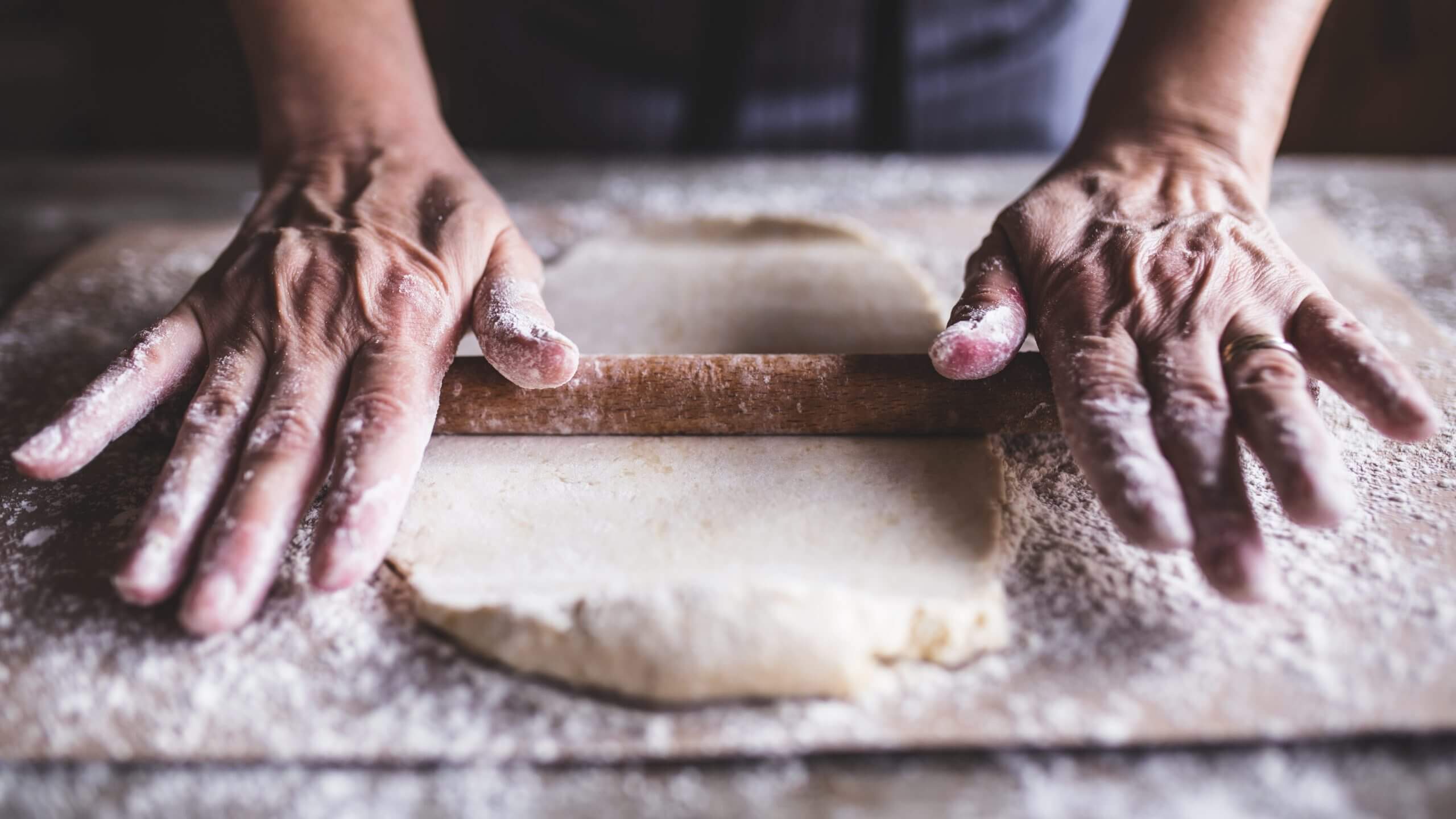 Strong hands masterfully rolling dough covered in flour on a wooden cutting board.