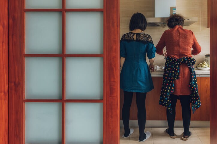 "Two women standing side by side as they focus on the cooking task at hand."