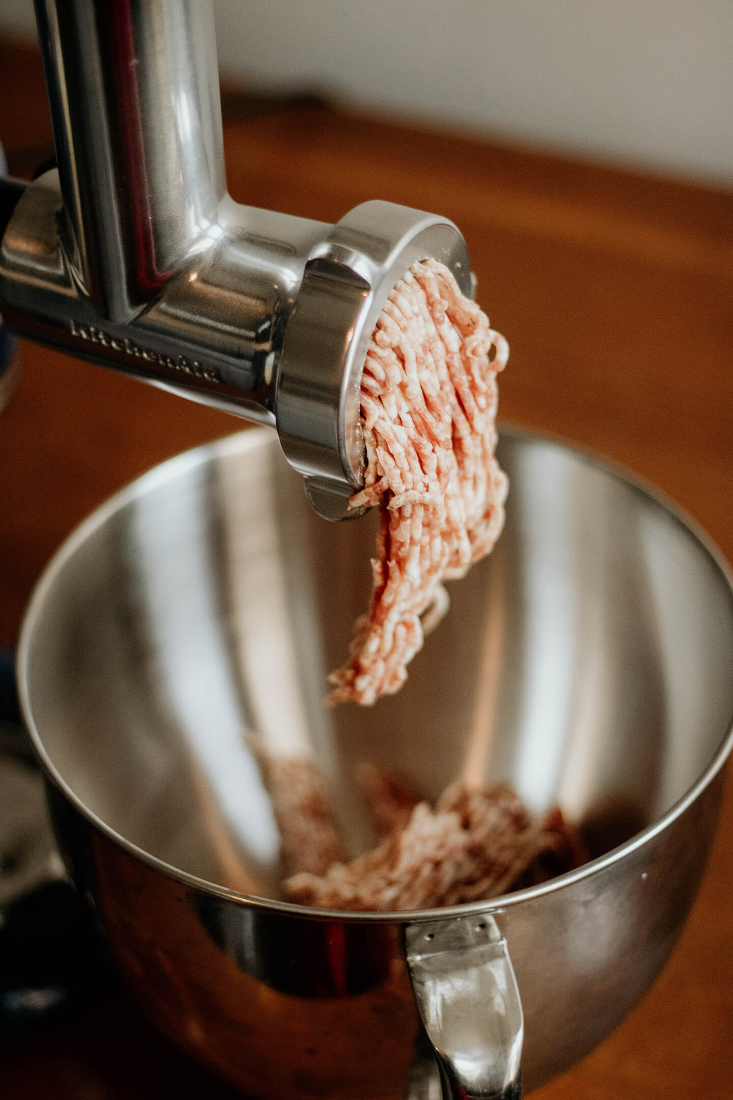 A KitchenAid® food grinder gently grinding meat into a bowl.