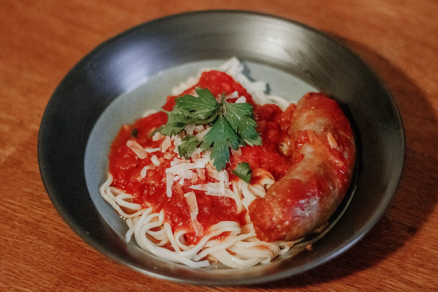 A bowl of freshly made pasta served with sauce and cooked sausage.