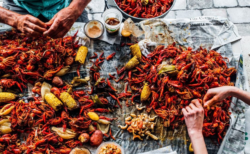 Seafood boil with shrimp, crab, crawfish and corn spread across newspaper laid out on a table.