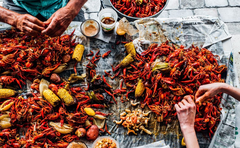 Seafood boil with shrimp, crab, crawfish and corn spread across newspaper laid out on a table.