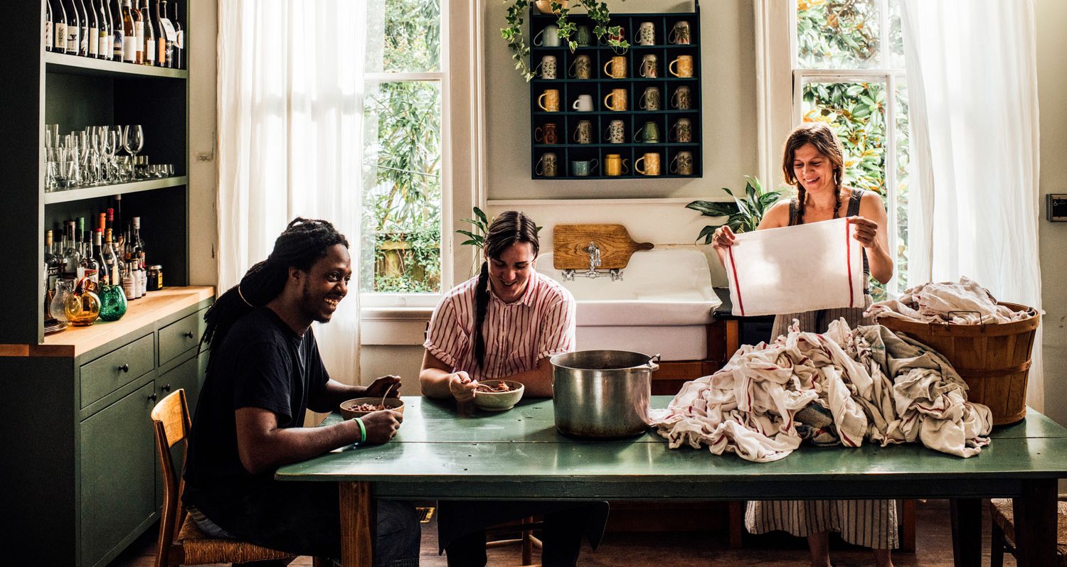 Chef Melissa Martin folding towels on a table with two friends eating mondays red beans.