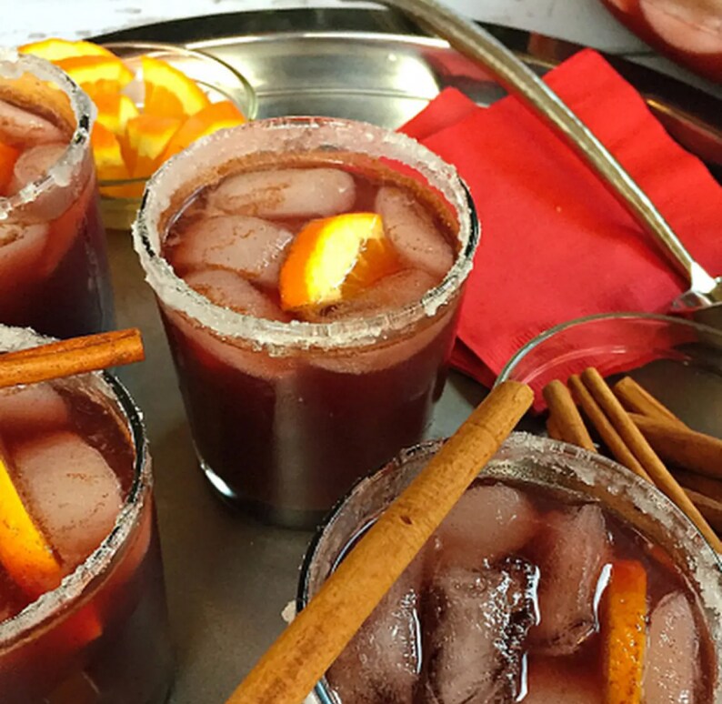 A cocktail with a salted rim, cinnamon sticks and orange slices.