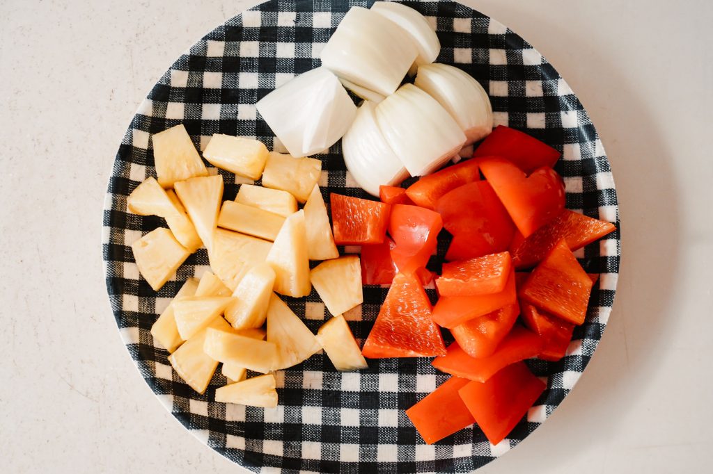 A plate of chopped onions, pineapples and red bell peppers.