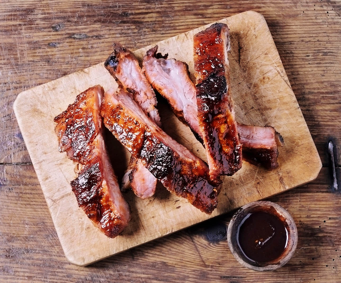A sliced rack of barbeque ribs resting on a wooden cutting board.