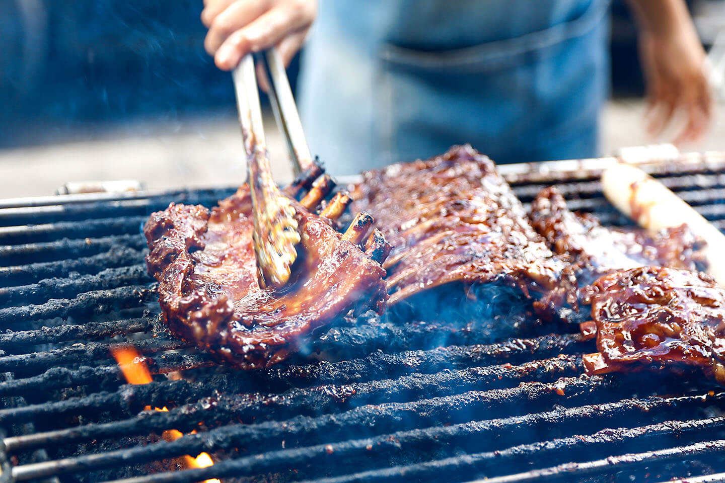A rack of juicy ribs being turned over by tongs on a hot grill.