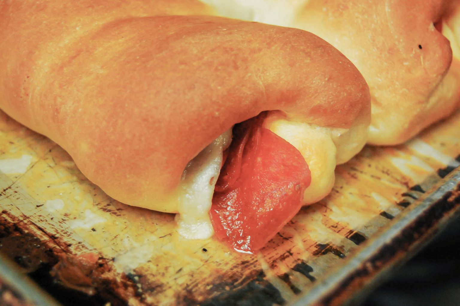 Cheese and pepperoni oozing out of a pepperoni roll.