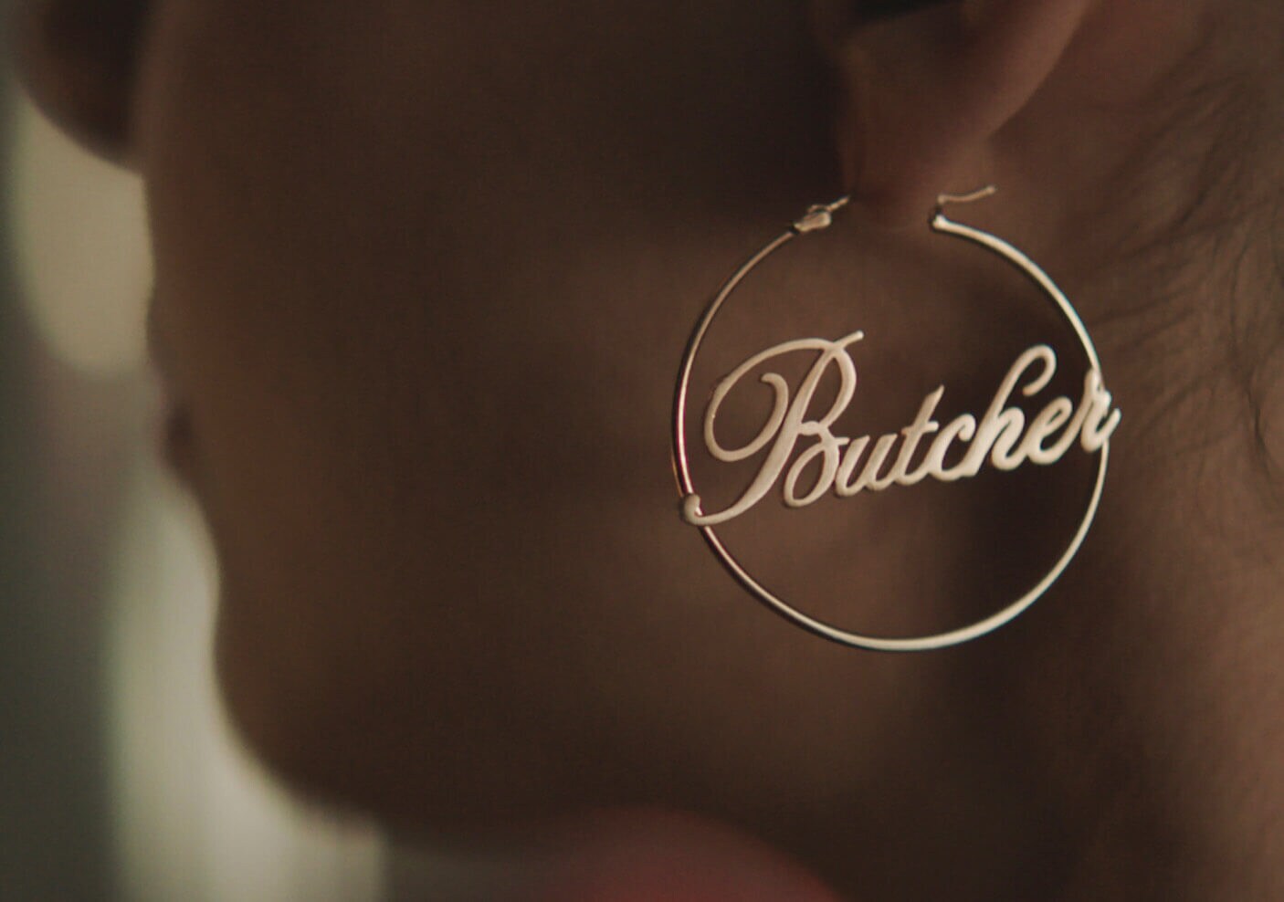 A golden hoop earring with a cursive Butcher in center.