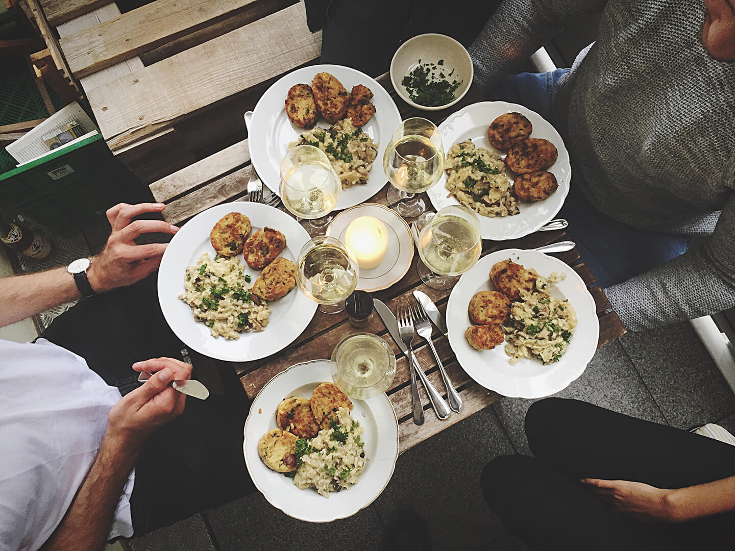 A circle of friends seated arounding a small table filled with food.