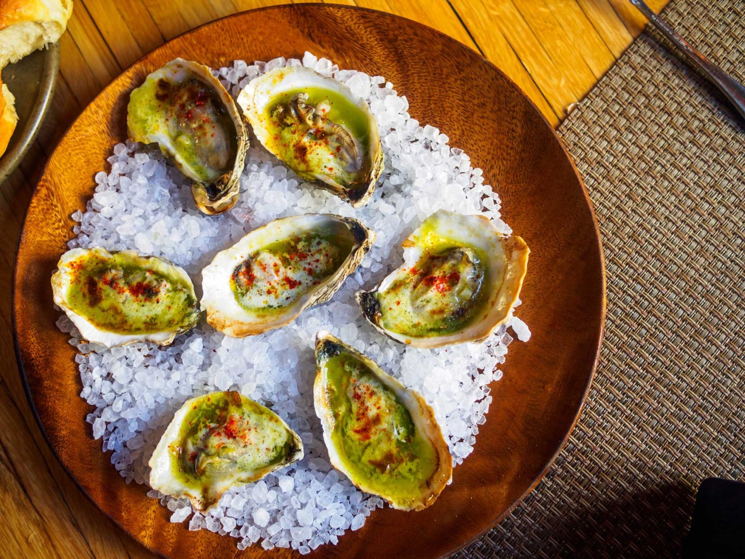 A wooden plate filled with seasoned oyster halves.