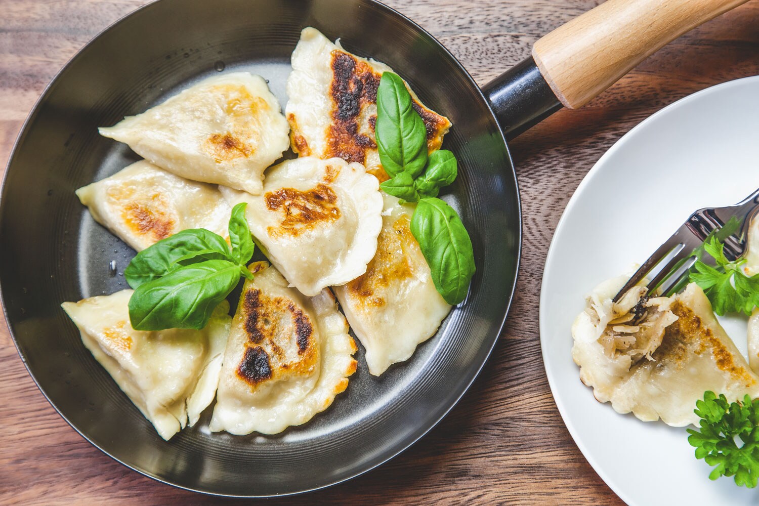 A pan filled with fried pierogies garnished with basil.