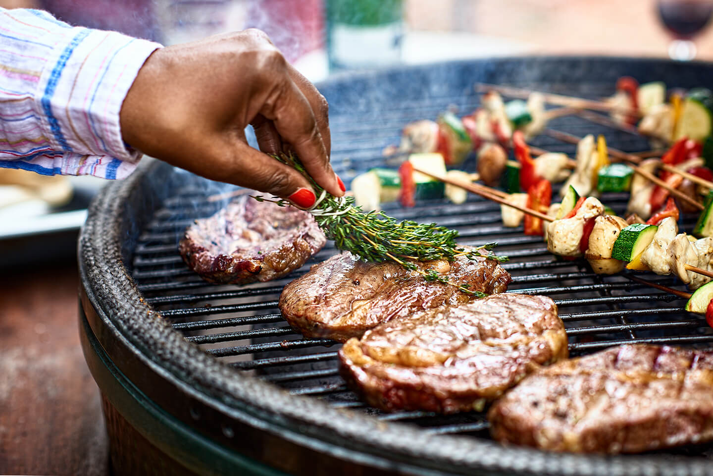 A hand basting grilled steaks in olive oil with a tied bunch of thyme.