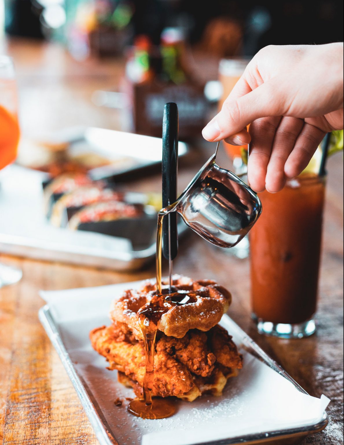 A person pouring syrup on a plate of chicken and waffles.