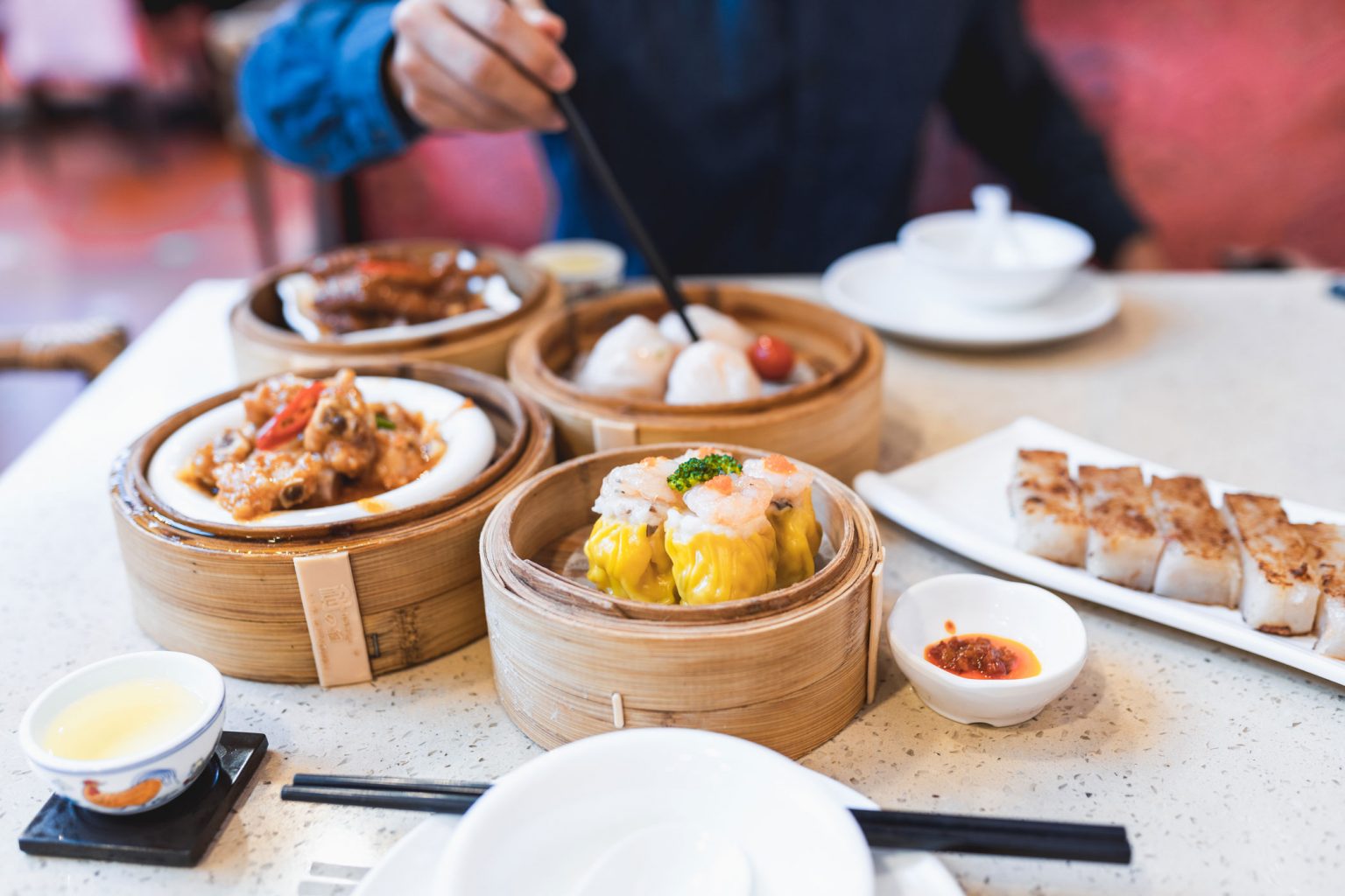A person enjoying lavish dishes of dim sum with another person.