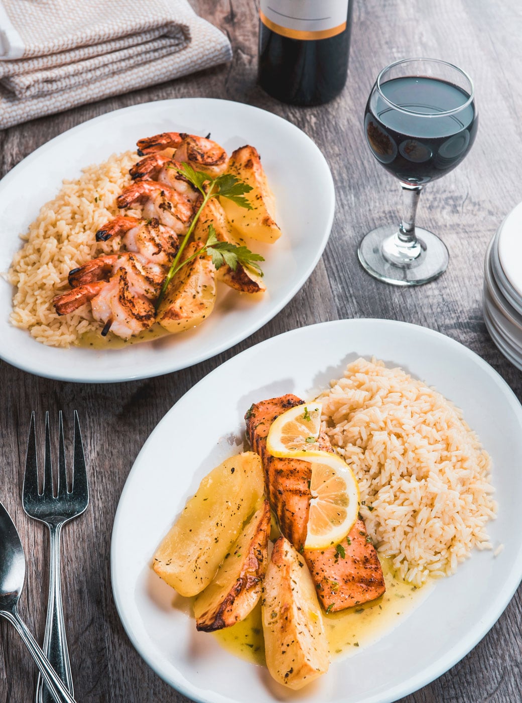 Two plates filled with seafood, rice and potatoes.
