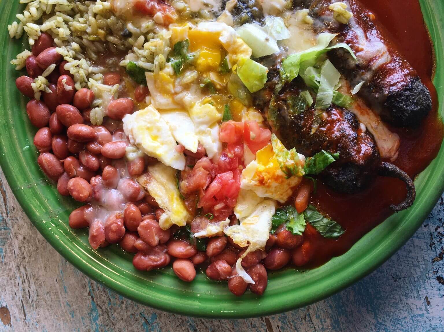 A green plate filled with beans, rice and grilled peppers topped with eggs and pico de gallo.