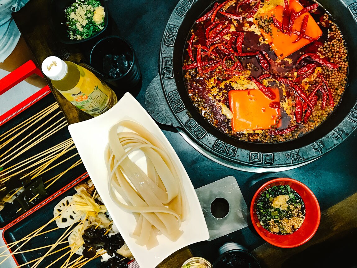 A white dish holding noodles next to a spicy steamboat.