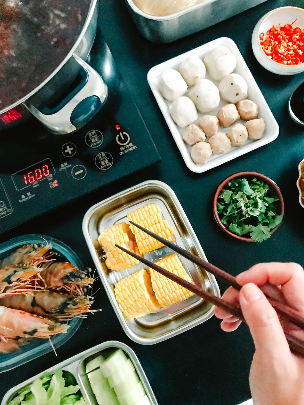 A black table with trays of raw corn, prawns and other ingredients.