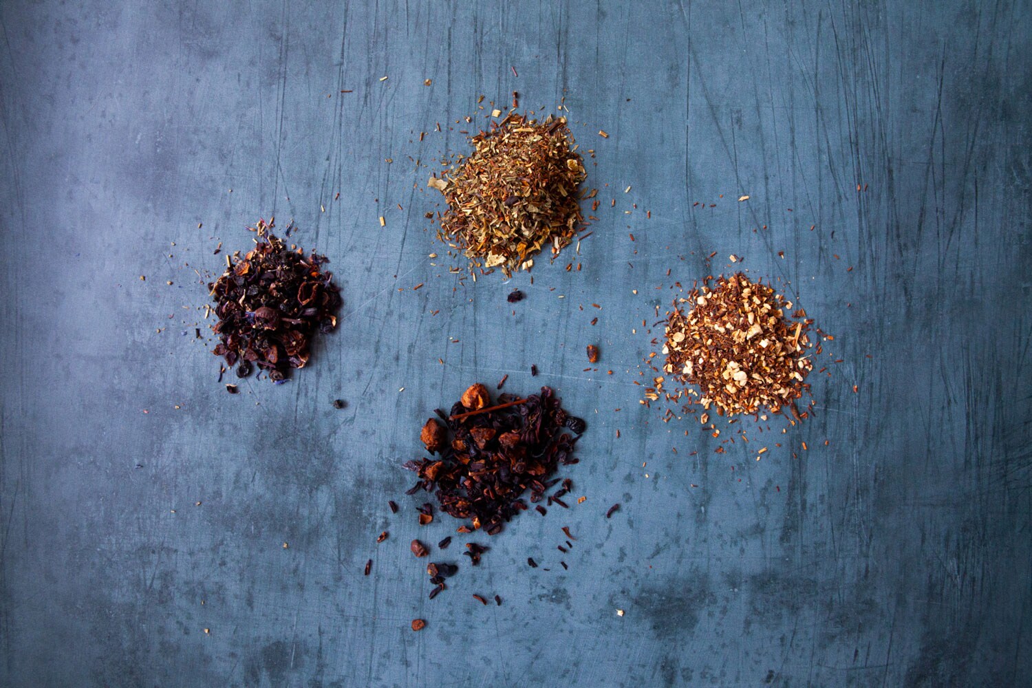 Four separate piles of various dried tea leaves.