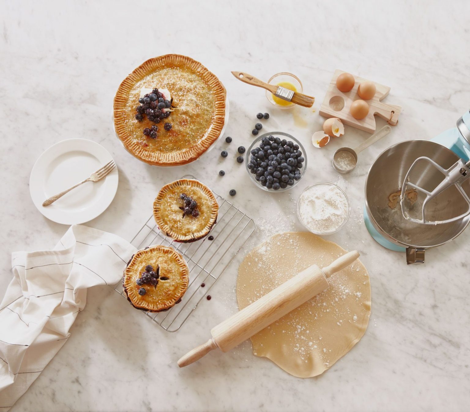 A set of three blueberry pies resting on a white kitchen counter.