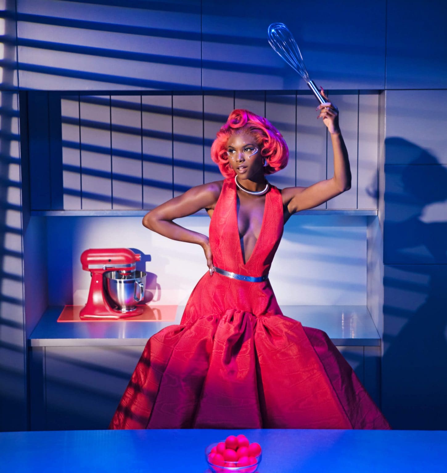 A model posing in a kitchen wearing Look Ten while holding a cooking tool near the Artisan® Series Stand Mixer on the countertop and a close-up of the KitchenAid® trim band on a model.