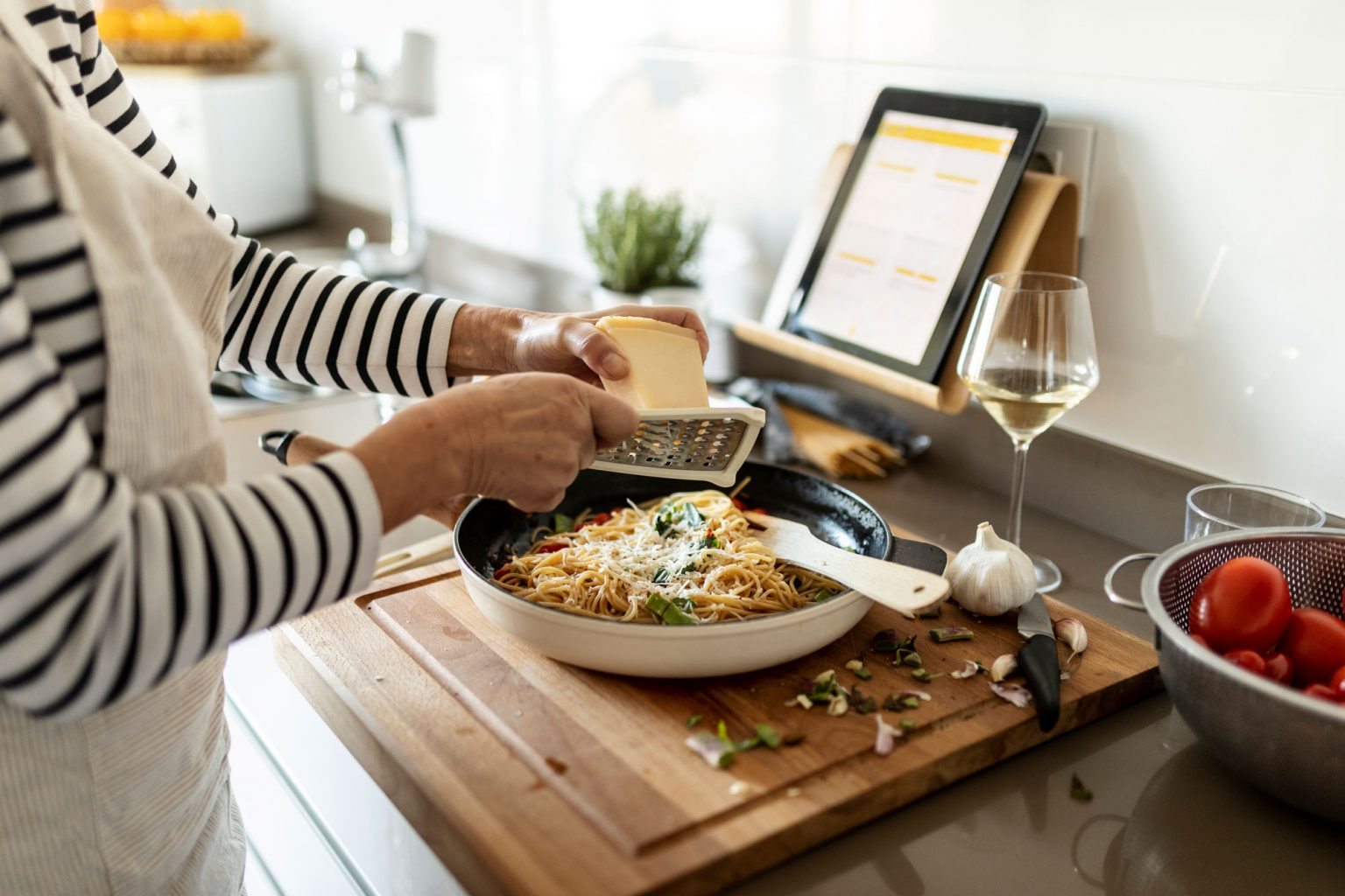 A person grating parmesan cheese into a skillet filled with spaghetti.