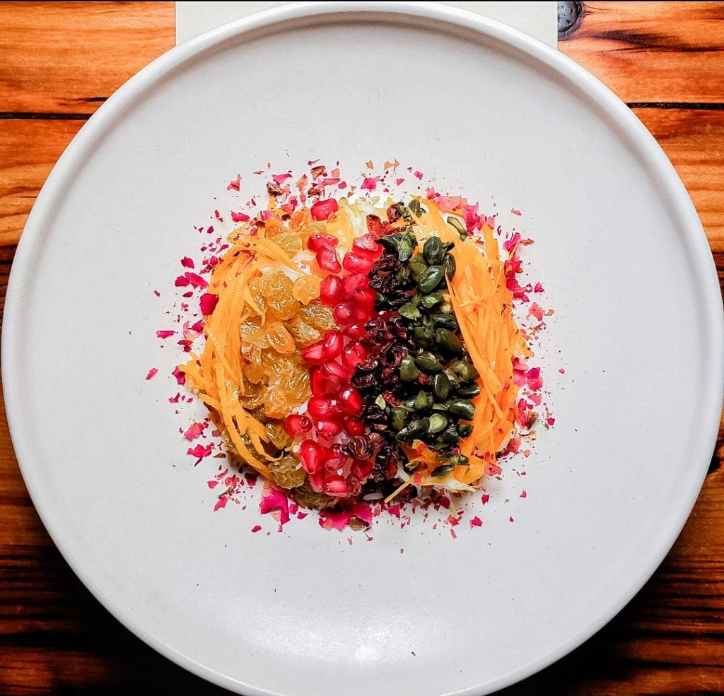 Pomegranate seeds, dried fruits, nuts and other delicacies served on a white plate.