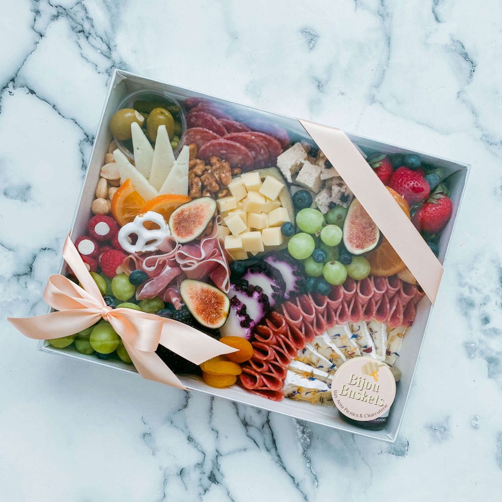 A picnic box filled with a variety of fruits, cheeses and nuts.