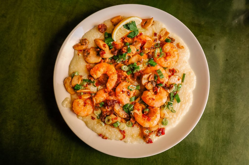 A large, flat bowl filled with shrimp and grits.
