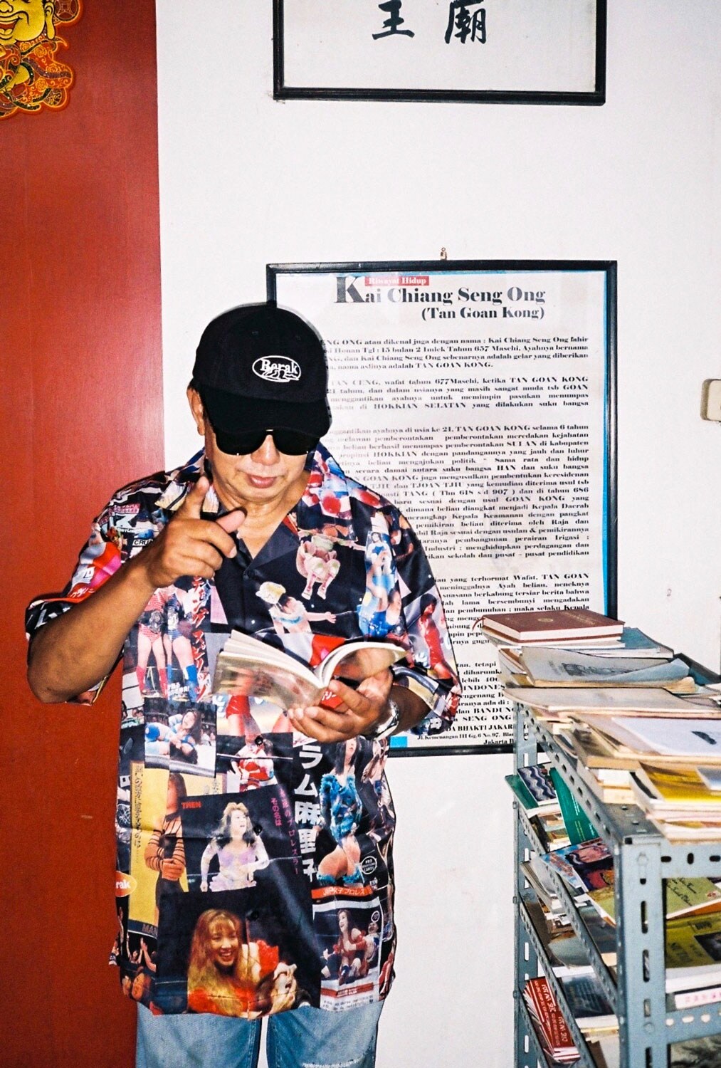Paulus Supomo in a retro shirt and sunglasses reading a magazine.