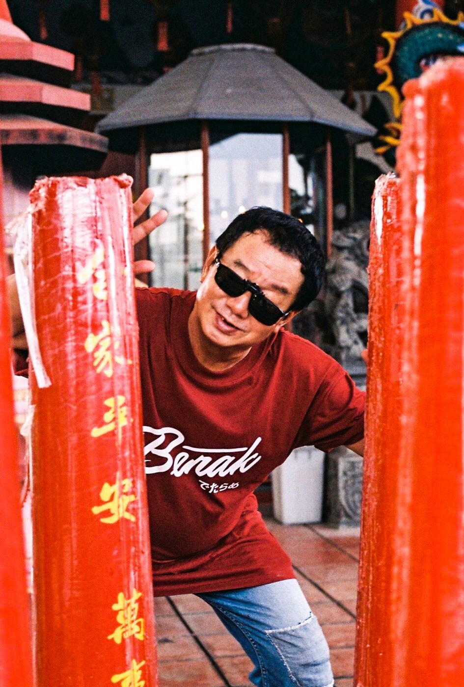 Paulus Supomo in sunglasses posing behind red pillar with yellow Chinese lettering on the street.