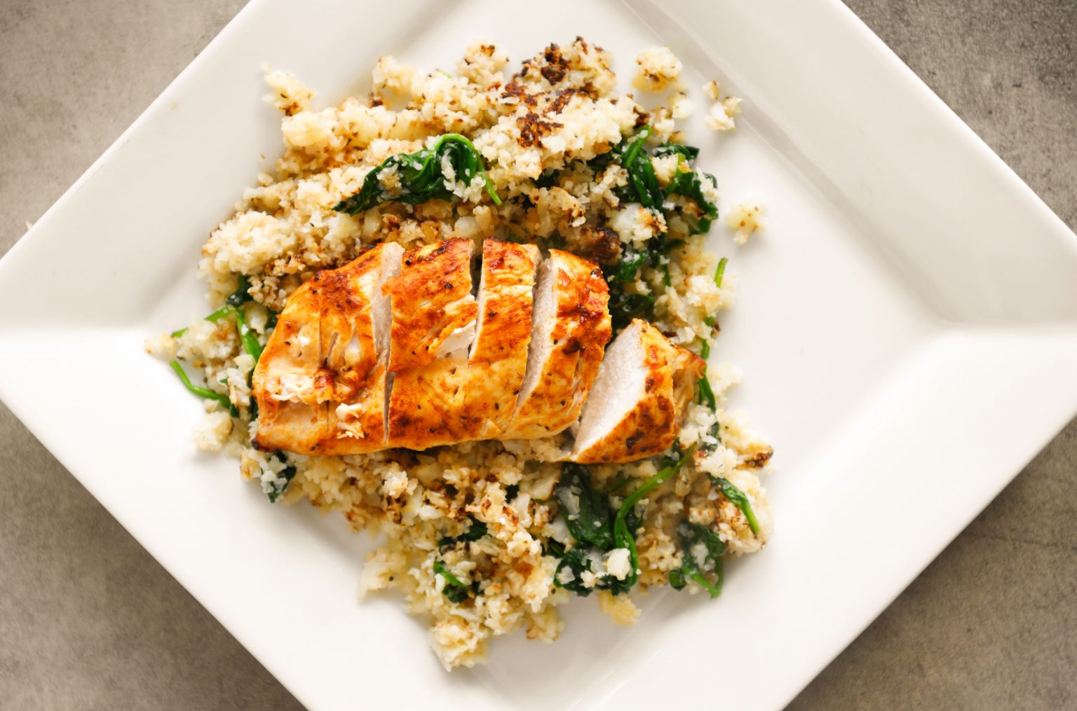 Sliced chicken resting on a bed of cauliflower rice.
