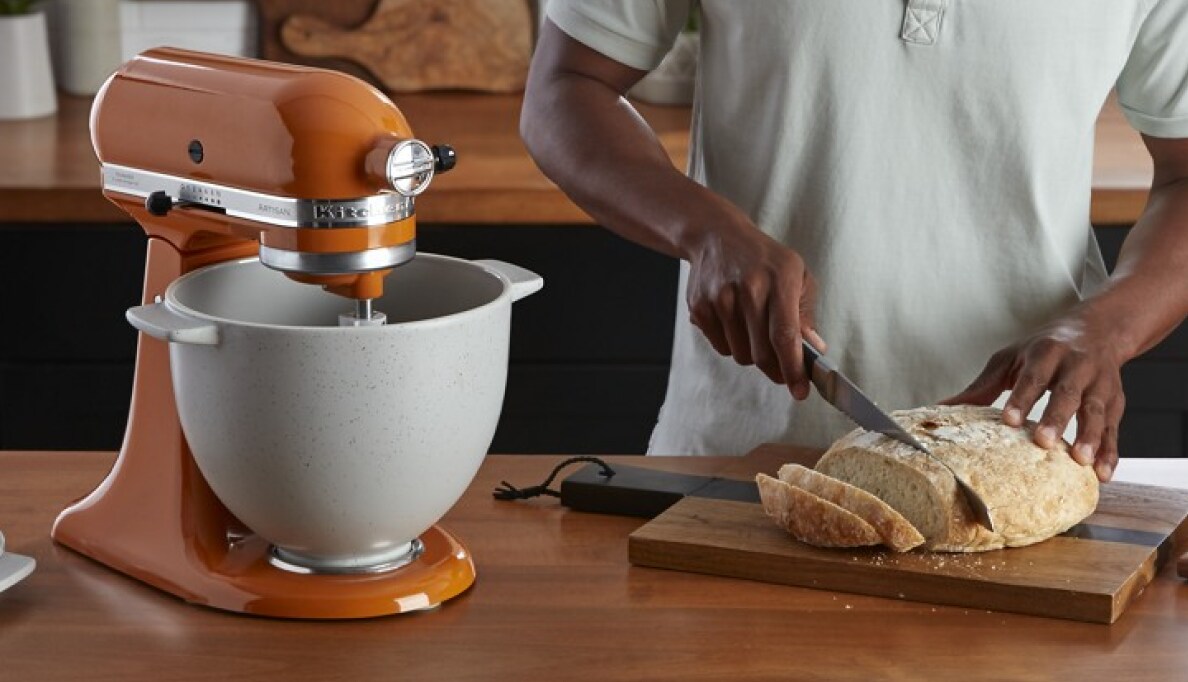 A person slicing bread next to a KitchenAid® stand mixer.