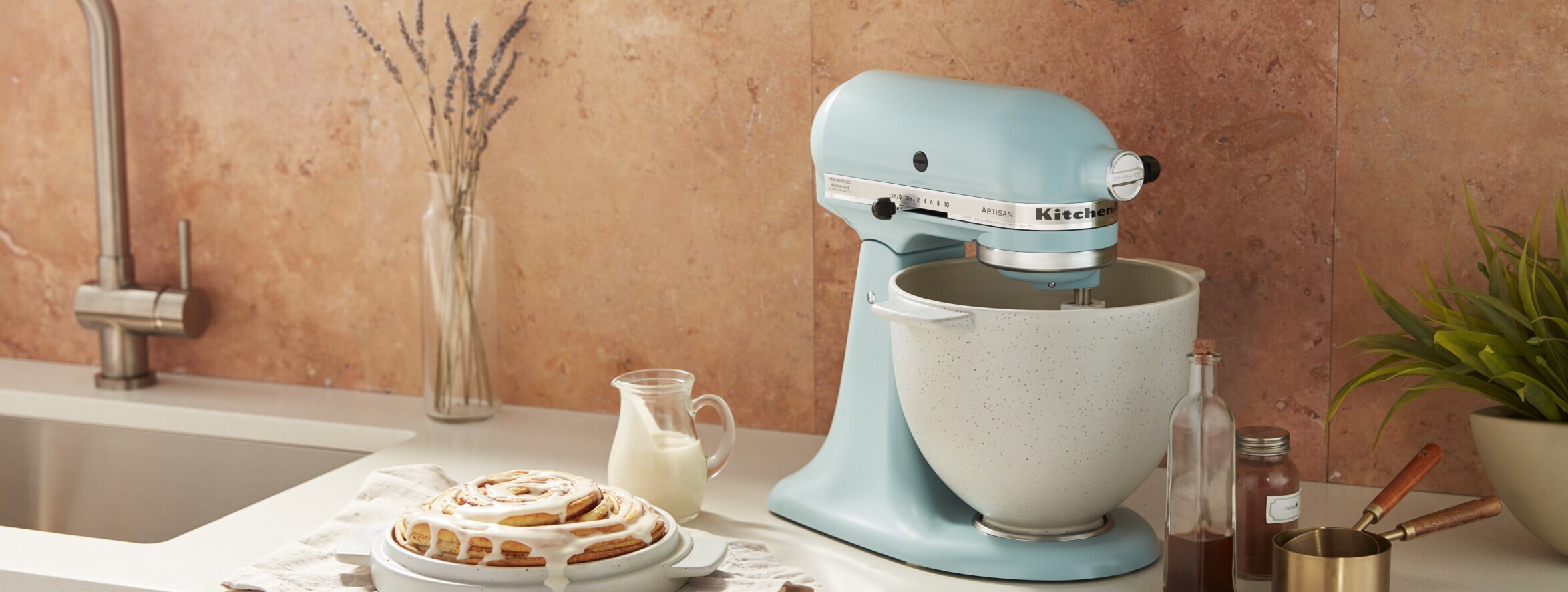 Glazed cinnamon bun beside a blue KitchenAid® Stand Mixer