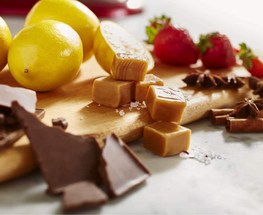 Chocolate, caramel, lemons and strawberries on a wooden cutting board.