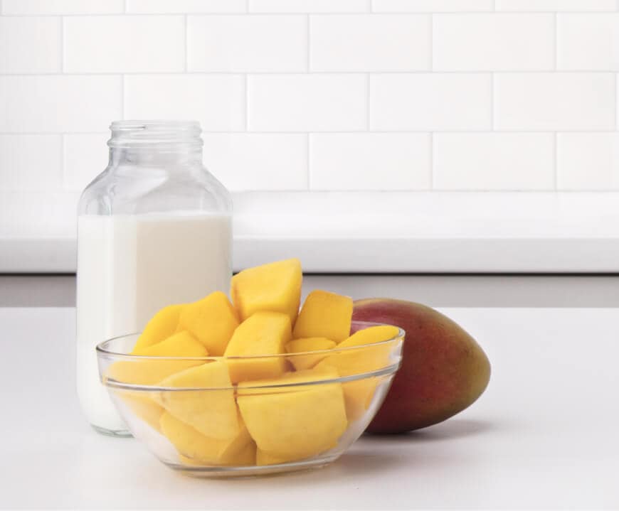 A bowl of sliced mango and a glass of milk.